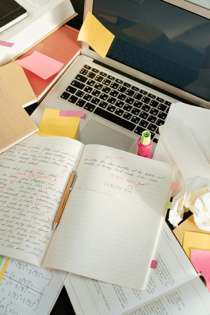 Messy creative workspace with open laptop, notebooks, and sticky notes.